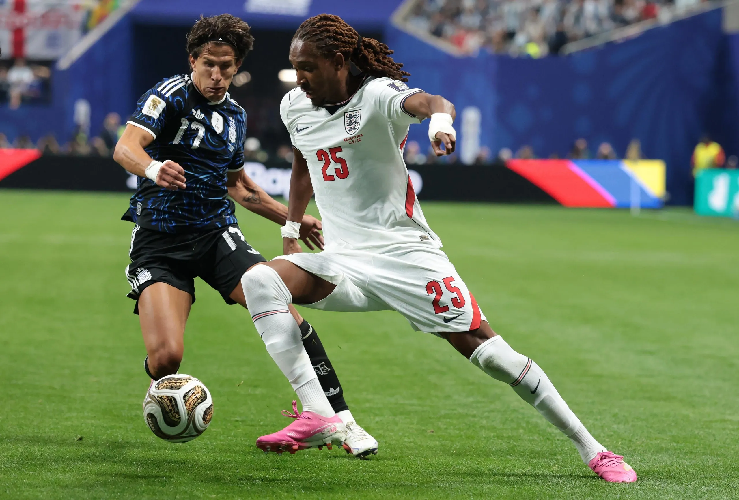 Djed Spence of England wearing a white jersey dribbles past an Argentina player wearing a blue jersey.