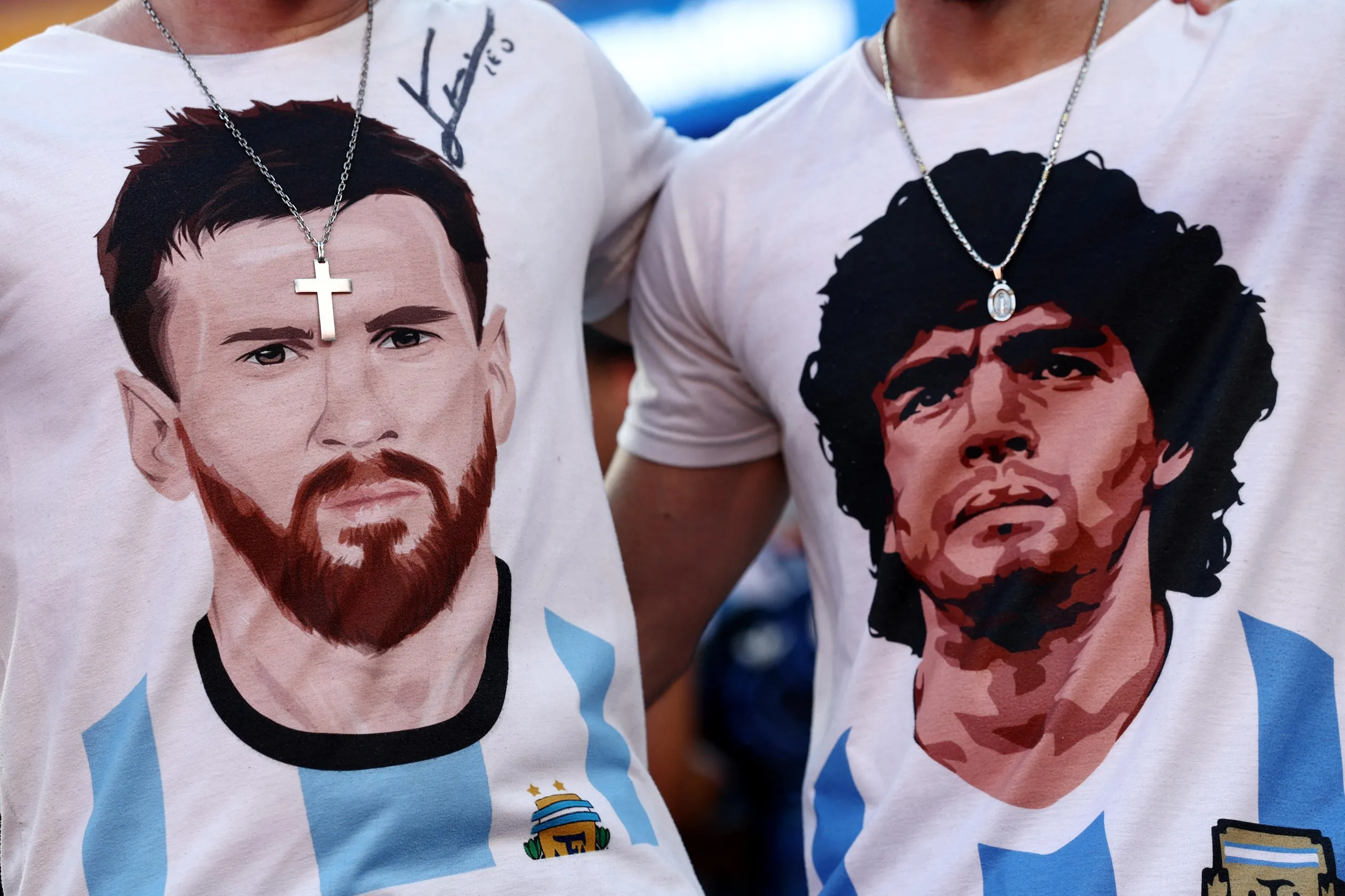 Two fans wear T-shirts with the faces of Lionel Messi and Diego Maradona.